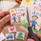 Parent cutting out a child's 'I love you dad' drawing with scissors, holding the finished Minigallery magnet