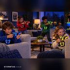 Four kids playing Stormtag laser tag in a living room at night, blasters and vests glowing blue, red, green and yellow